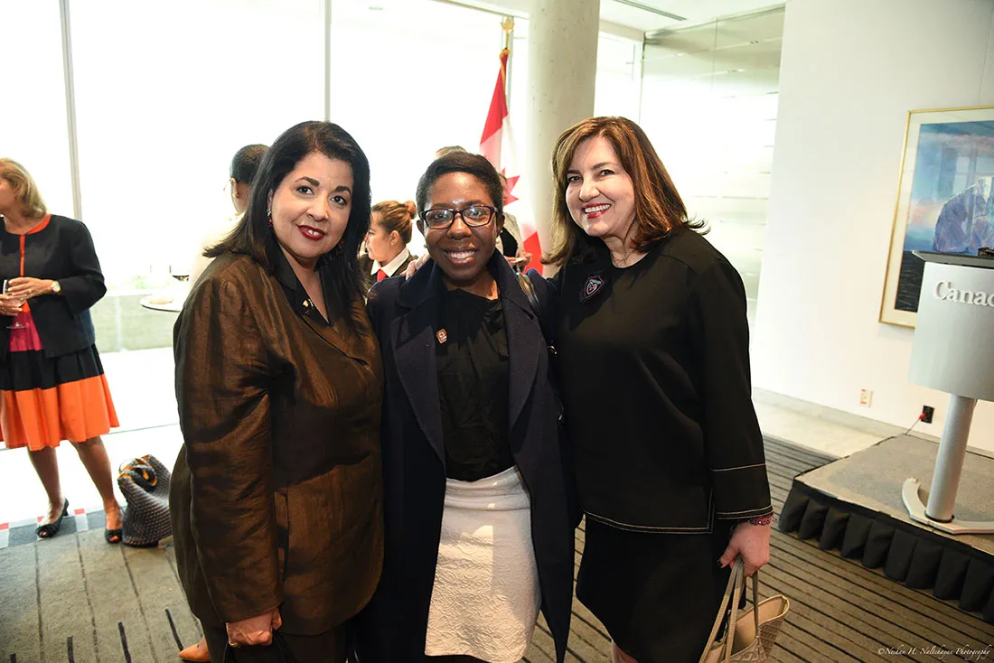 Tres mujeres asistentes al evento se paran juntas frente a la bandera canadiense.