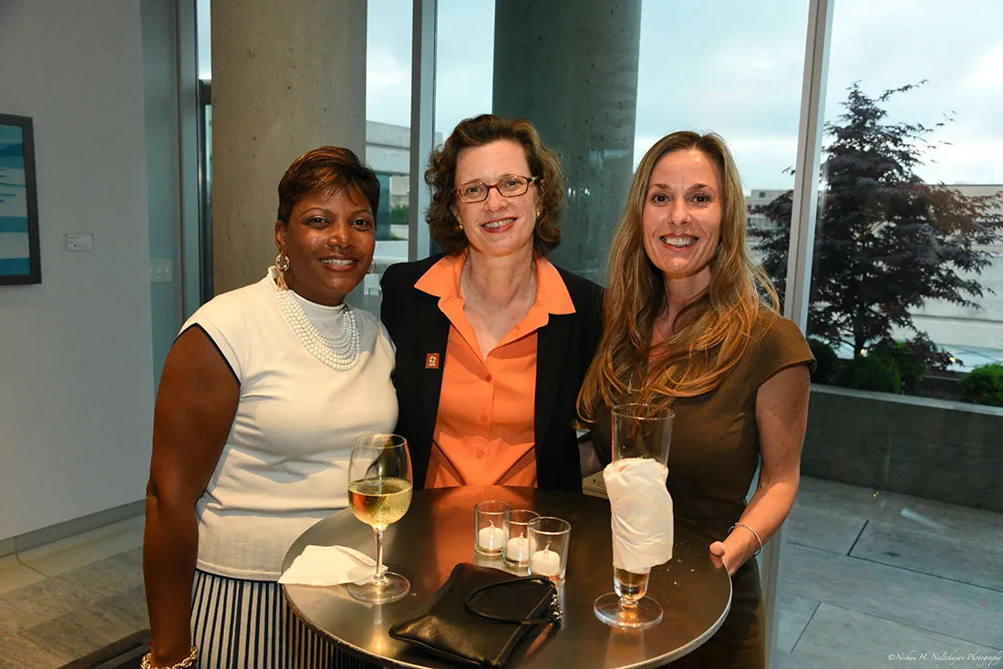 La directora ejecutiva de CARE, Michelle Nunn, con un broche de CARE naranja y una blusa naranja, posa con dos asistentes al evento.
