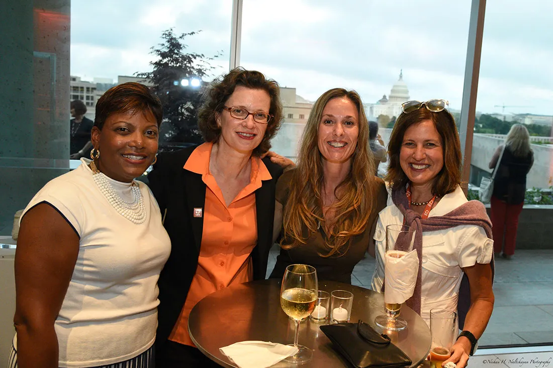 La directora ejecutiva de CARE, Michelle Nunn, con un broche de CARE naranja y una blusa naranja, posa con tres asistentes al evento.