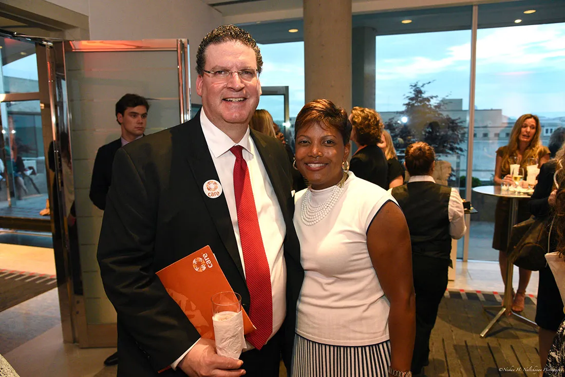 A man wearing a CARE pin and holding a CARE folder poses next to a woman.