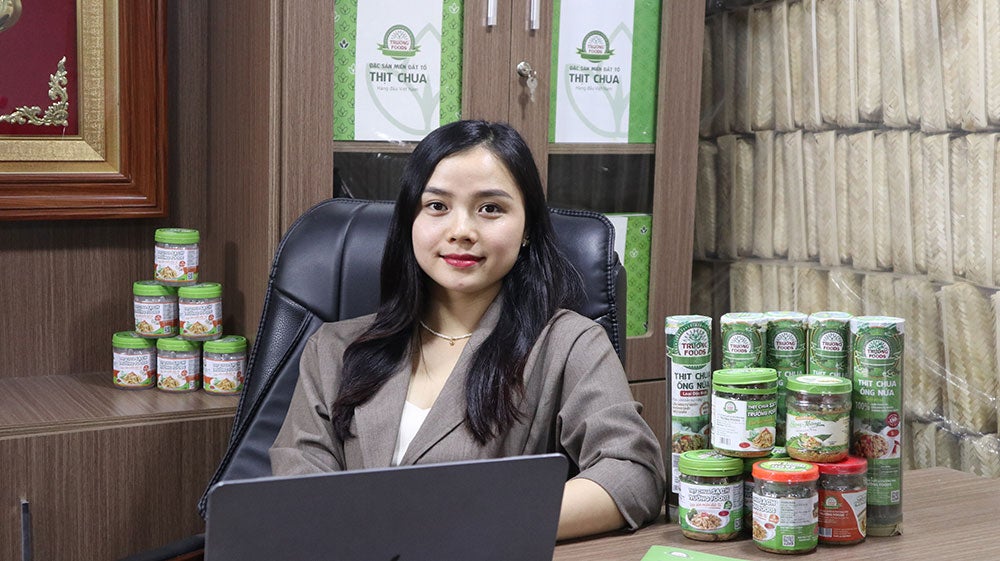 Nguyen Thi Hien sites at her desk, surrounded by canned goods.
