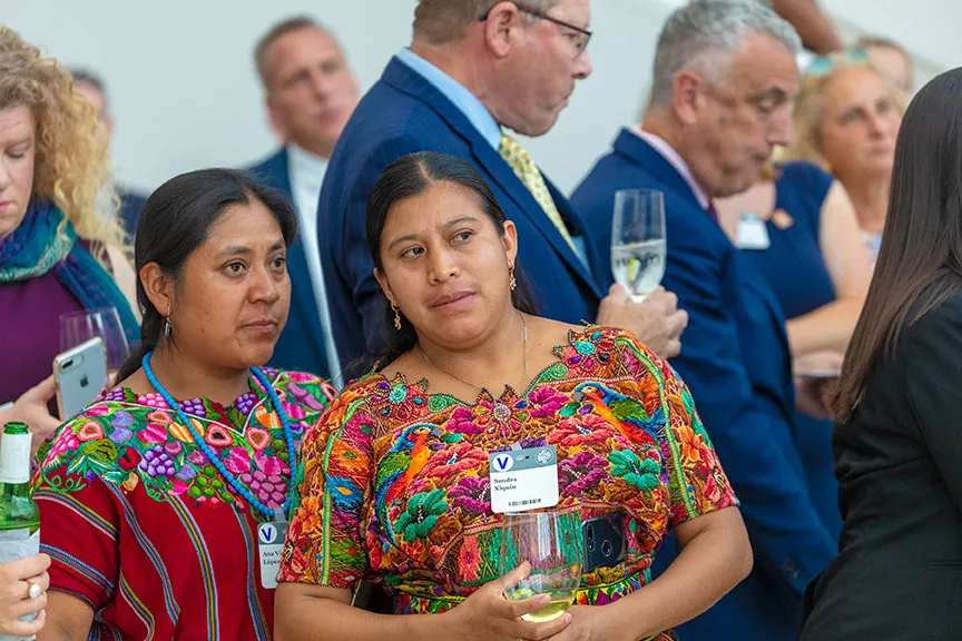 Two women wearing brightly patterned, embroidered outfits, talk.