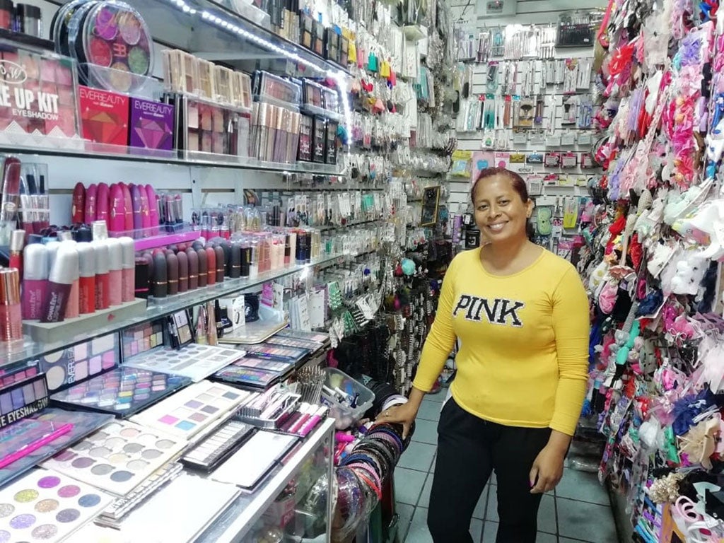 A woman wearing a yellow PINK sweater stands in an aisle of a store, surrounded by beauty products.