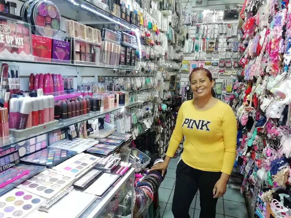 Uma mulher vestindo um suéter amarelo PINK está no corredor de uma loja, cercada por produtos de beleza.