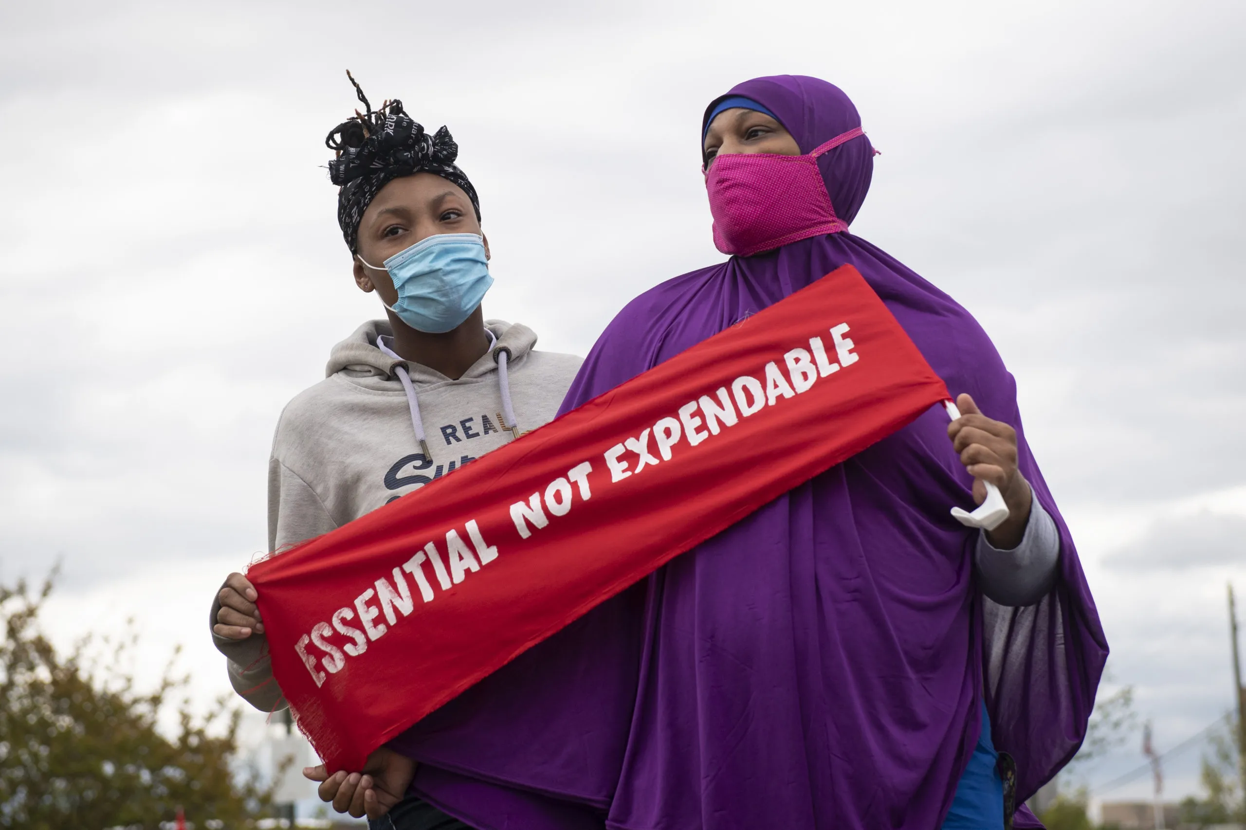 Duas mulheres com máscaras seguram uma placa que diz