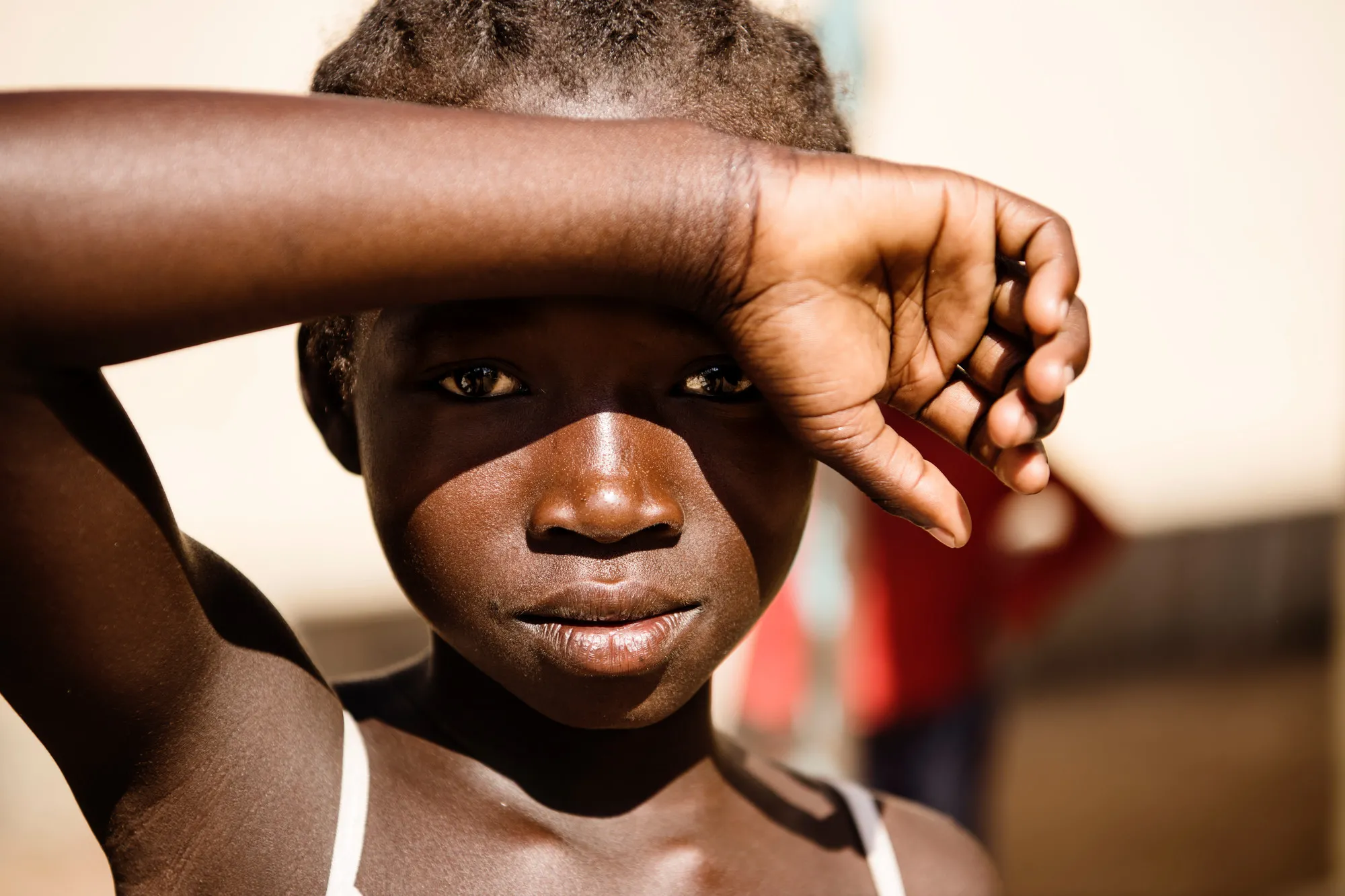 A girl shields her eyes from the sun with her arm over her brow.