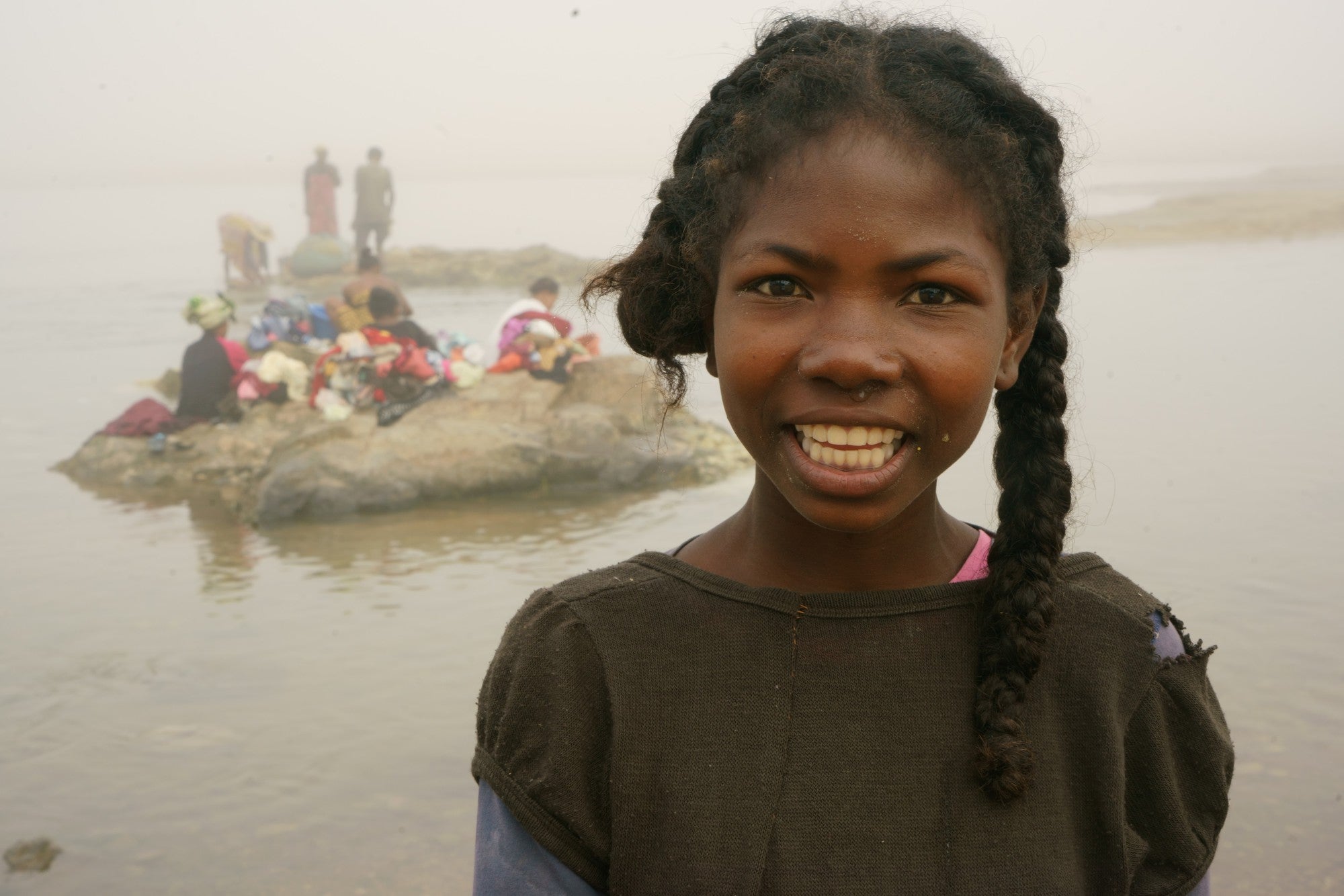 Uma garota está em frente a um rio com uma pequena ilha visível atrás dela.