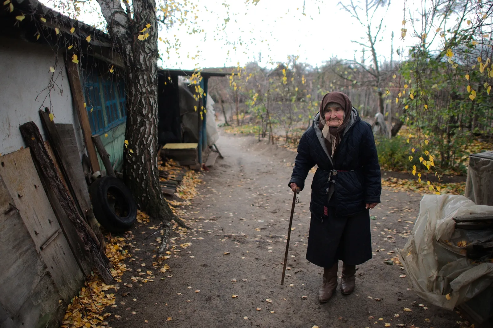an elderly women walks on the street while holding a cane.