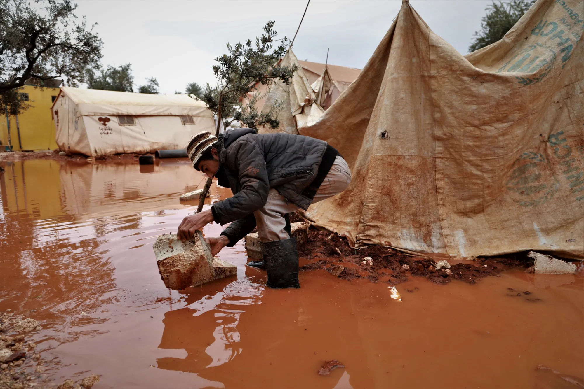 A man bends down outside of a flooded tent in a camp.