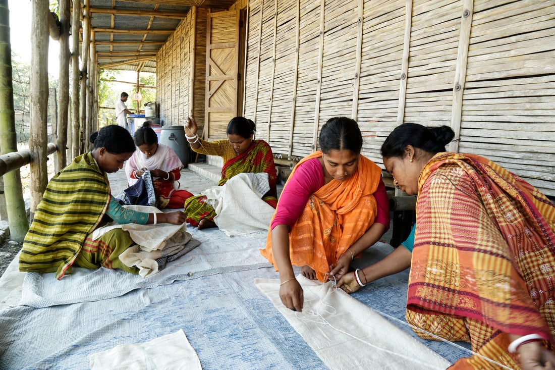 A group of women kneel on a porch working with white fabric.
