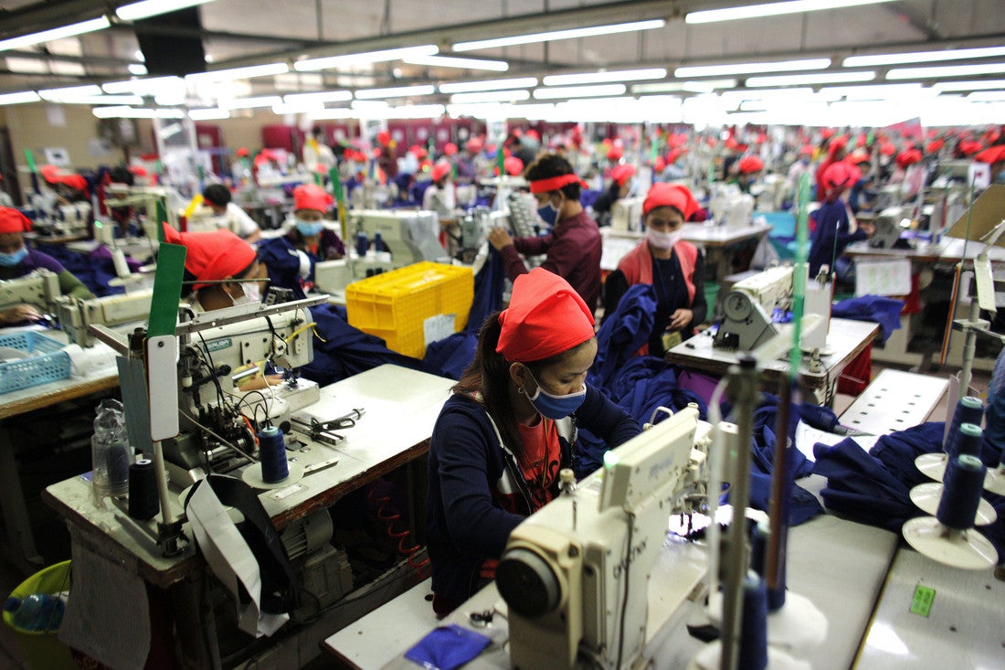 Un gran edificio lleno de mujeres sentadas en escritorios individuales con máquinas de coser. Cada empleado lleva un pañuelo rojo.