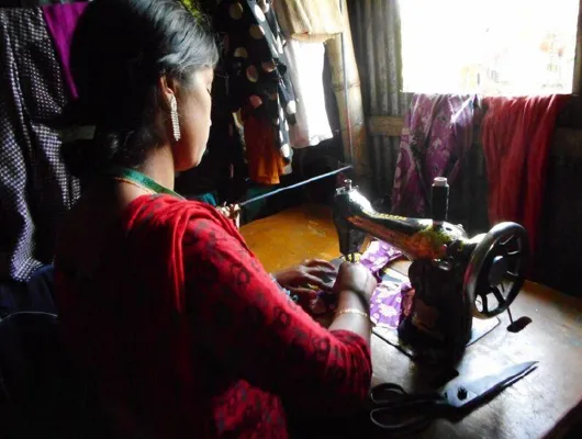 A woman in red clothing is sewing a piece of cloth.