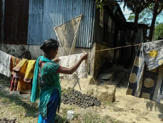 A lady in blue clothing is drying a piece of cloth outside.