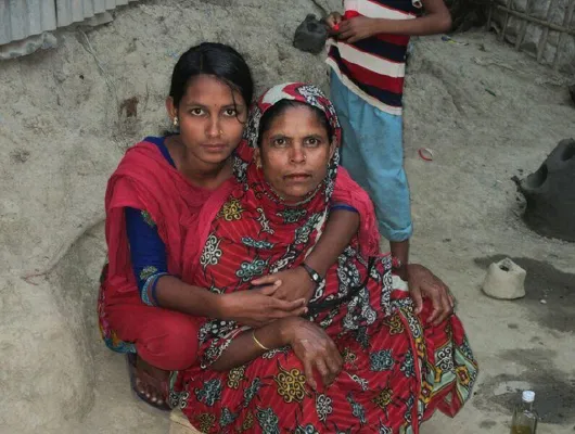 A young lady wearing a pink scarf holds her mother who wears a red piece of cloth.