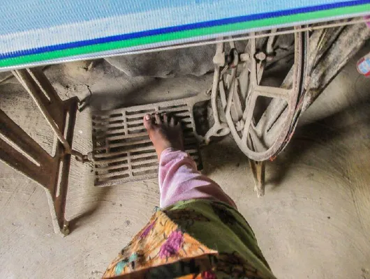 A foot of a woman wearing a pink and green cloth is on the pedal of a sewing machine.