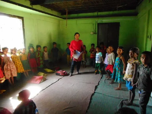 A lady in red clothing stands in the middle of young children while holding a book.