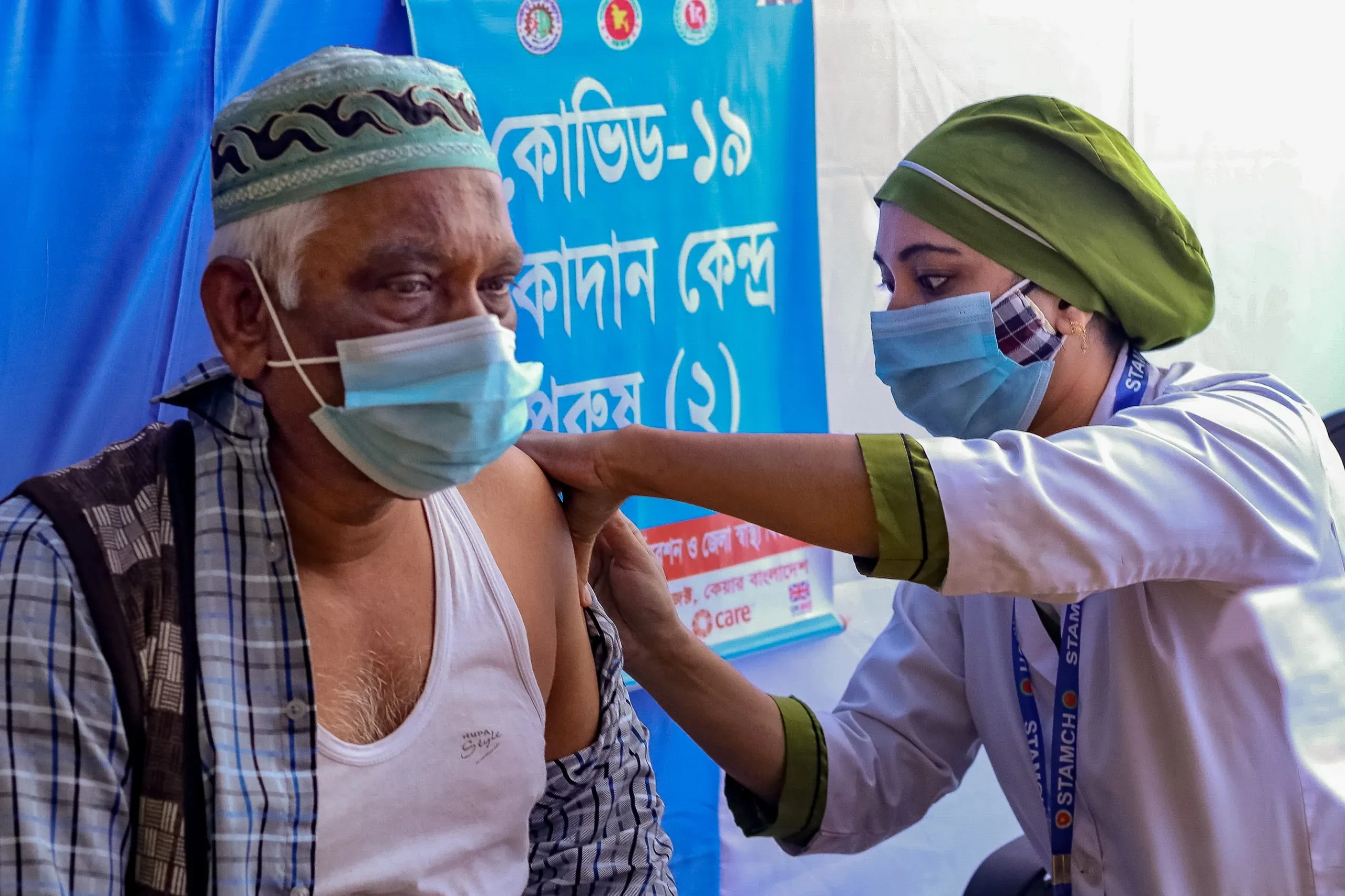 Both wearing masks, a woman health care worker gives a vaccine to a man.