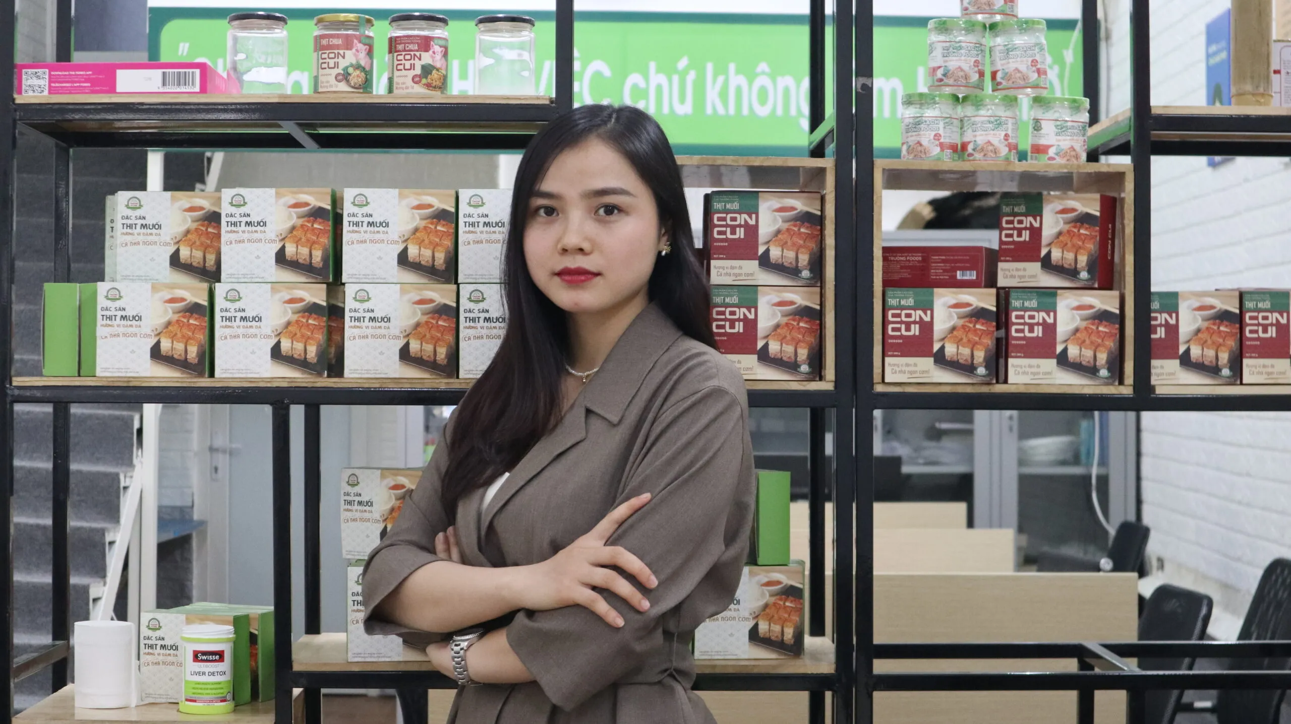 A woman stands in front of shelves stocked with food.