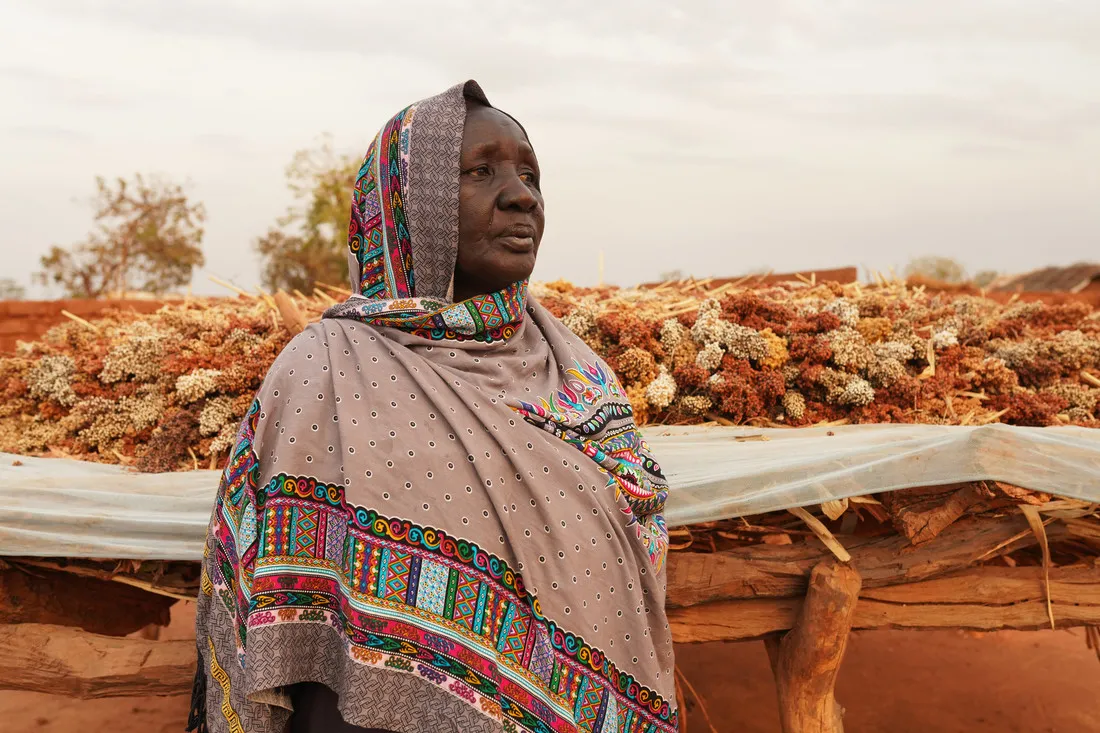 Uma mulher afetada pela crise humanitária do Sudão do Sul olha para o horizonte. Atrás dela, flores secas foram colocadas sobre uma lona branca.