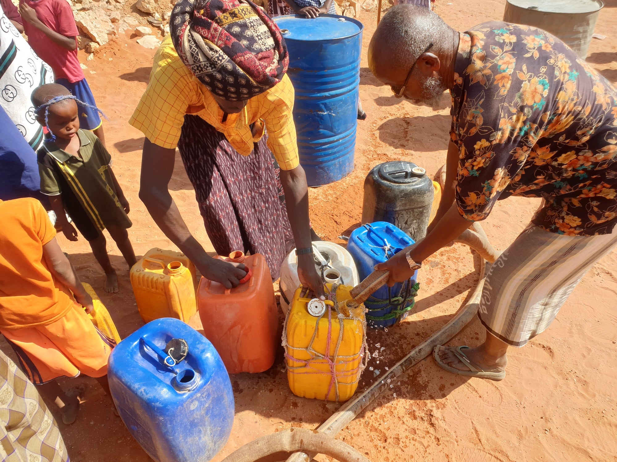 A family fills jerry cans with water.