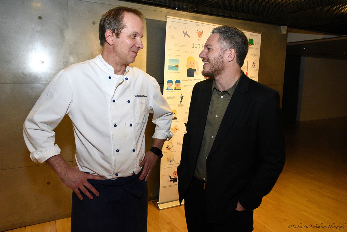 Two men, one in chef costume and another in a black suit, are talking to each other