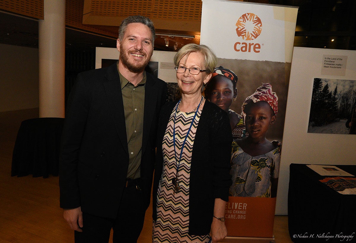 Ambassador Kristi Kauppi and a man in a black suit are standing in front of a CARE banner