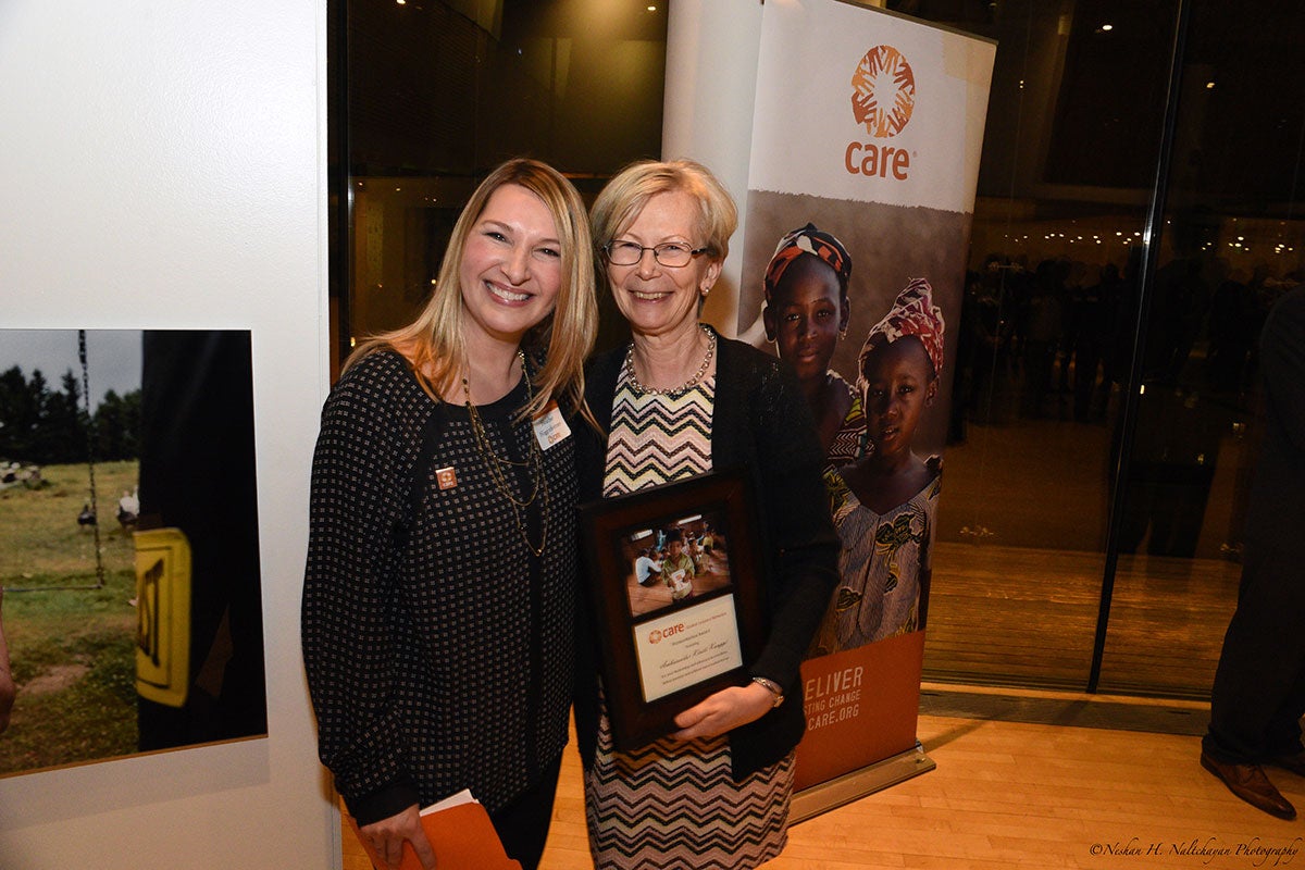 Ambassador Kristi Kauppi is holding a CARE award standing next to a woman in a black and white shirt in front of a CARE banner