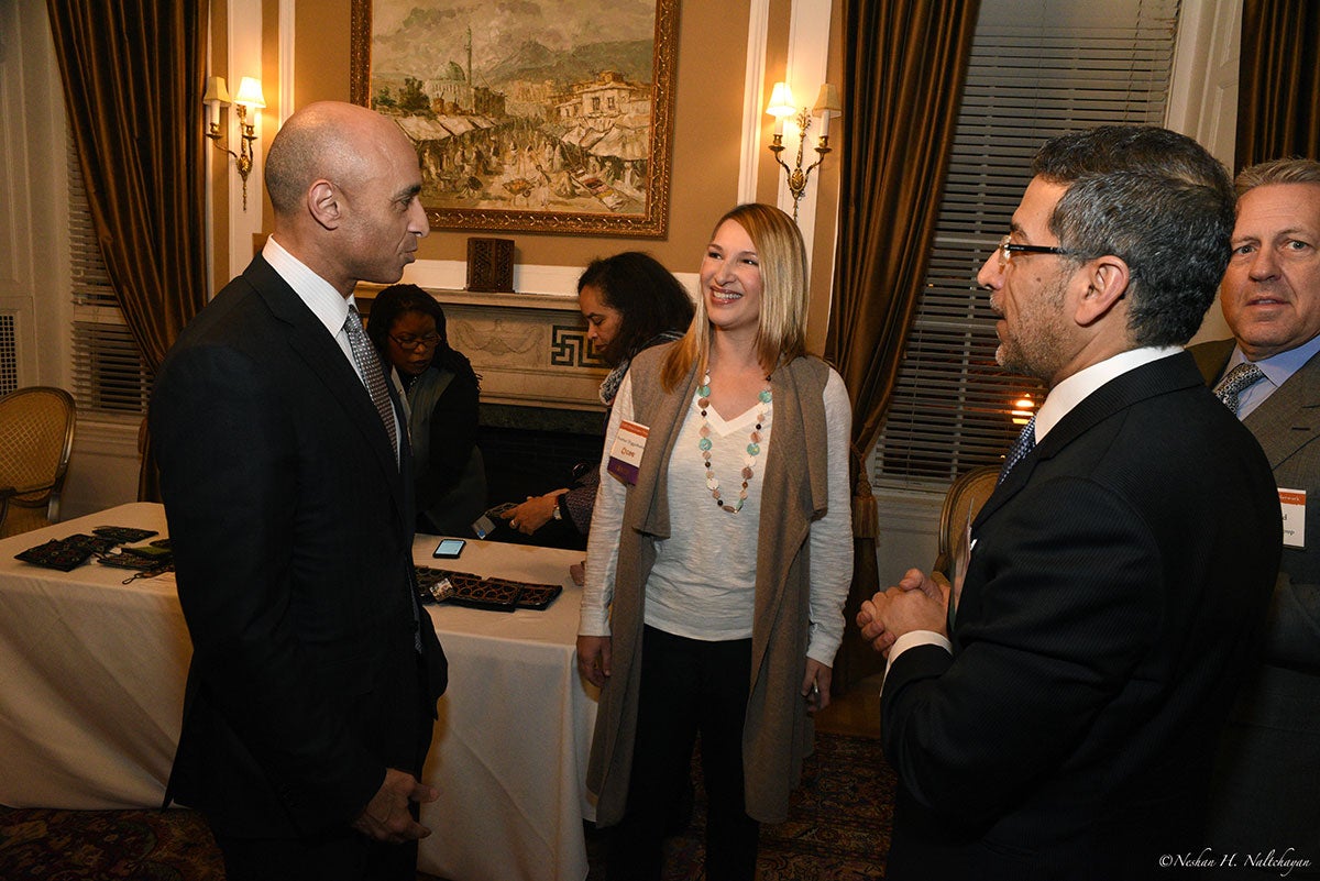 A man in black suit is talking to a smiling woman in a white shirt next to a man in a black suit