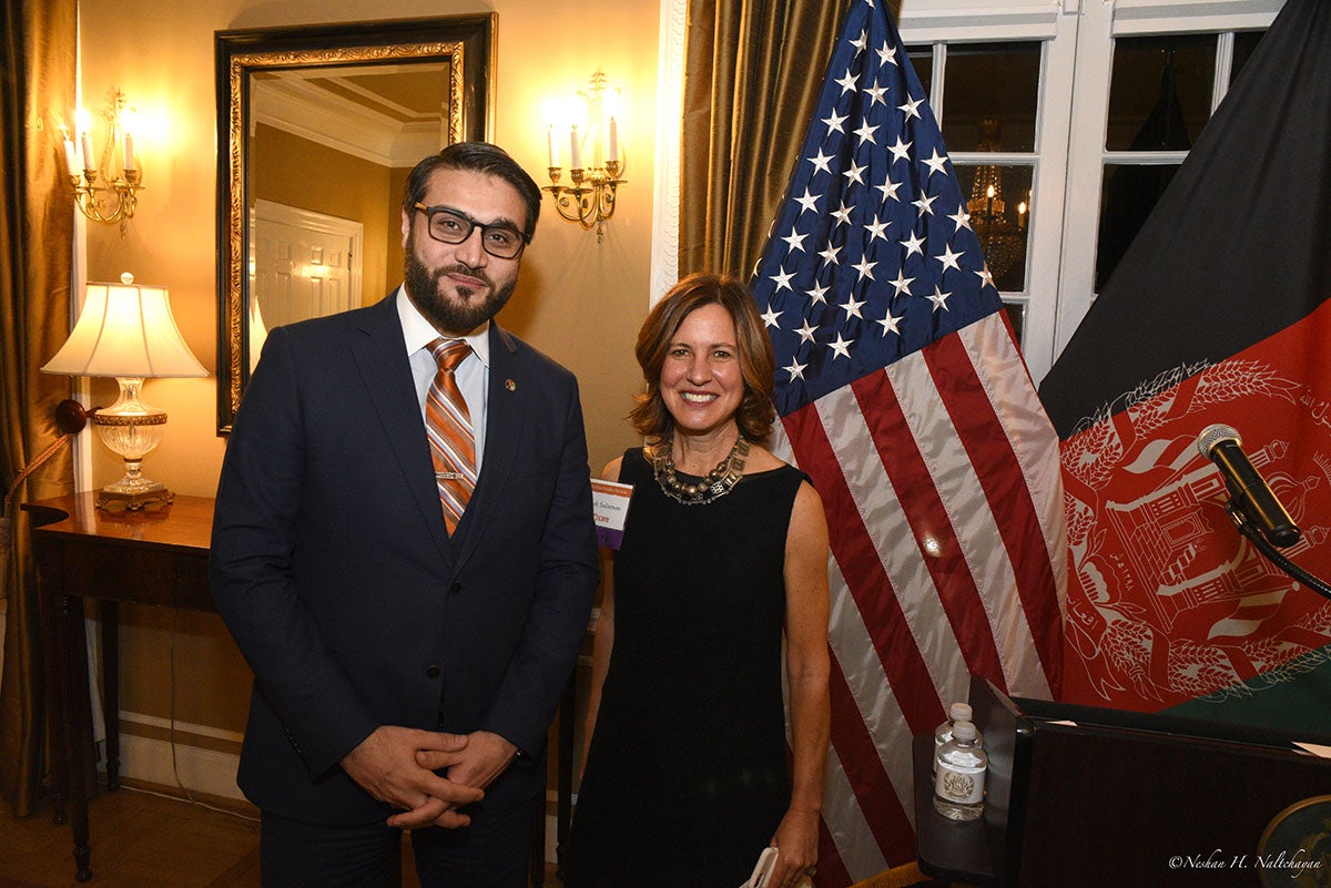 Ambassador Hamdullah Mohib stands next to a woman in a black dress in front of both the American and Afghan flags