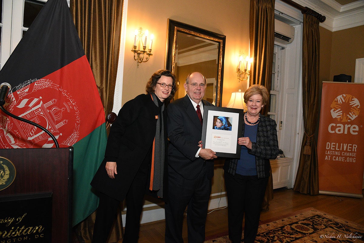 A man stands holding a CARE award between CARE CEO Michelle Nunn and a woman in a blue shit and black and gray coat