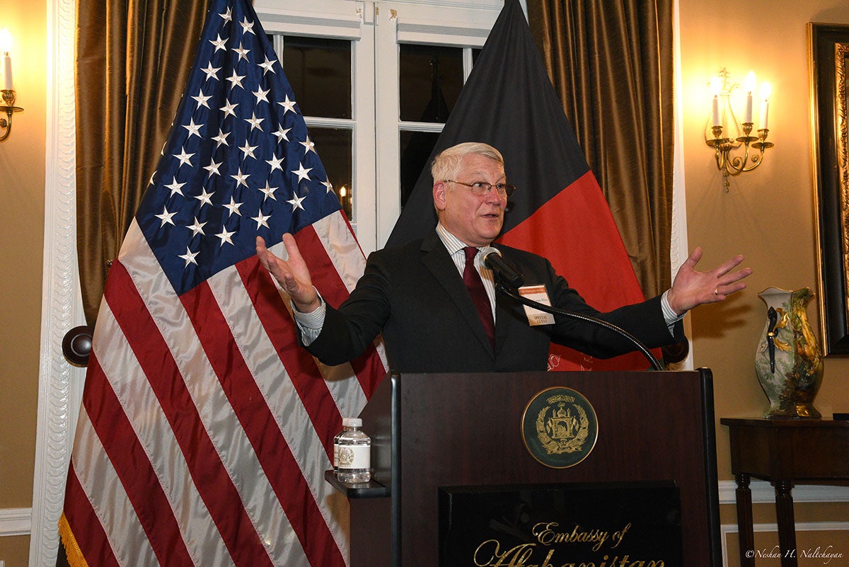 A man in a black suit is giving a speech with the US and Afghan flags in the background
