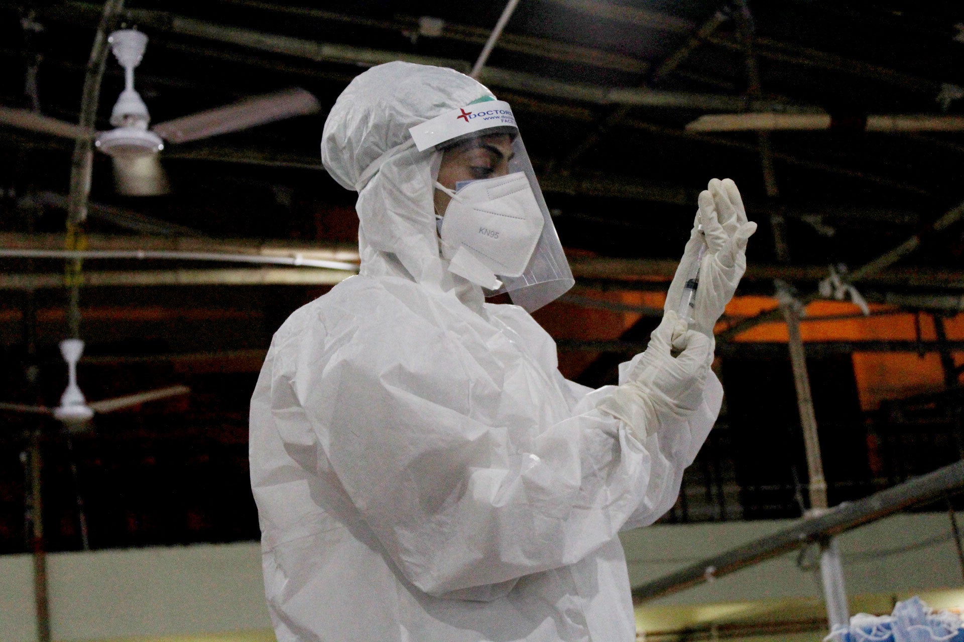 A health care worker in PPE holds a syringe.