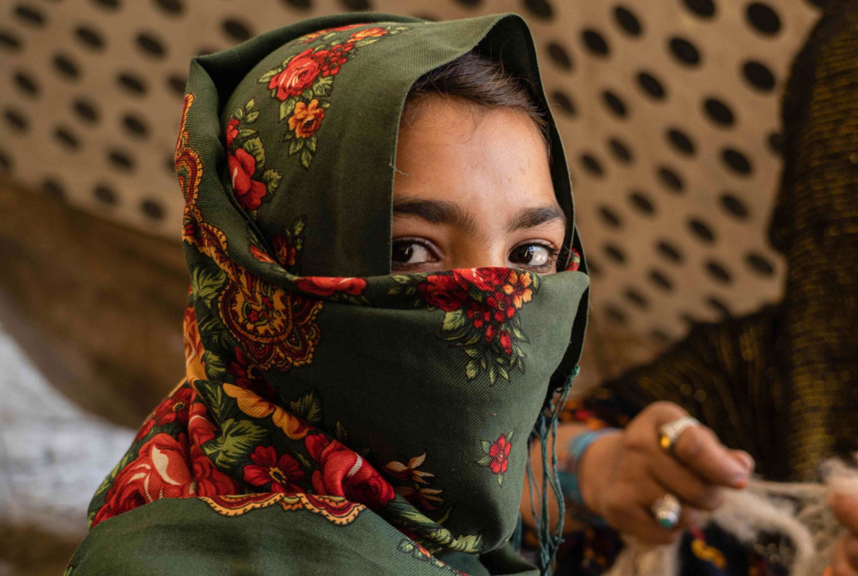 A young Afghan woman looks over her shoulder. Most of her face is covered by a green and red floral headscarf.
