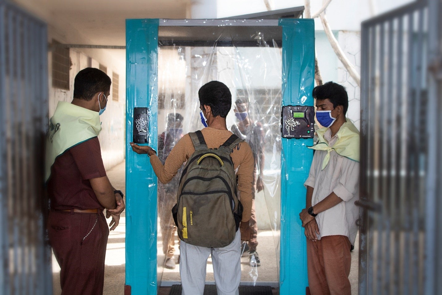 Tres niños yemeníes con máscaras parados frente a una puerta de saneamiento en su escuela