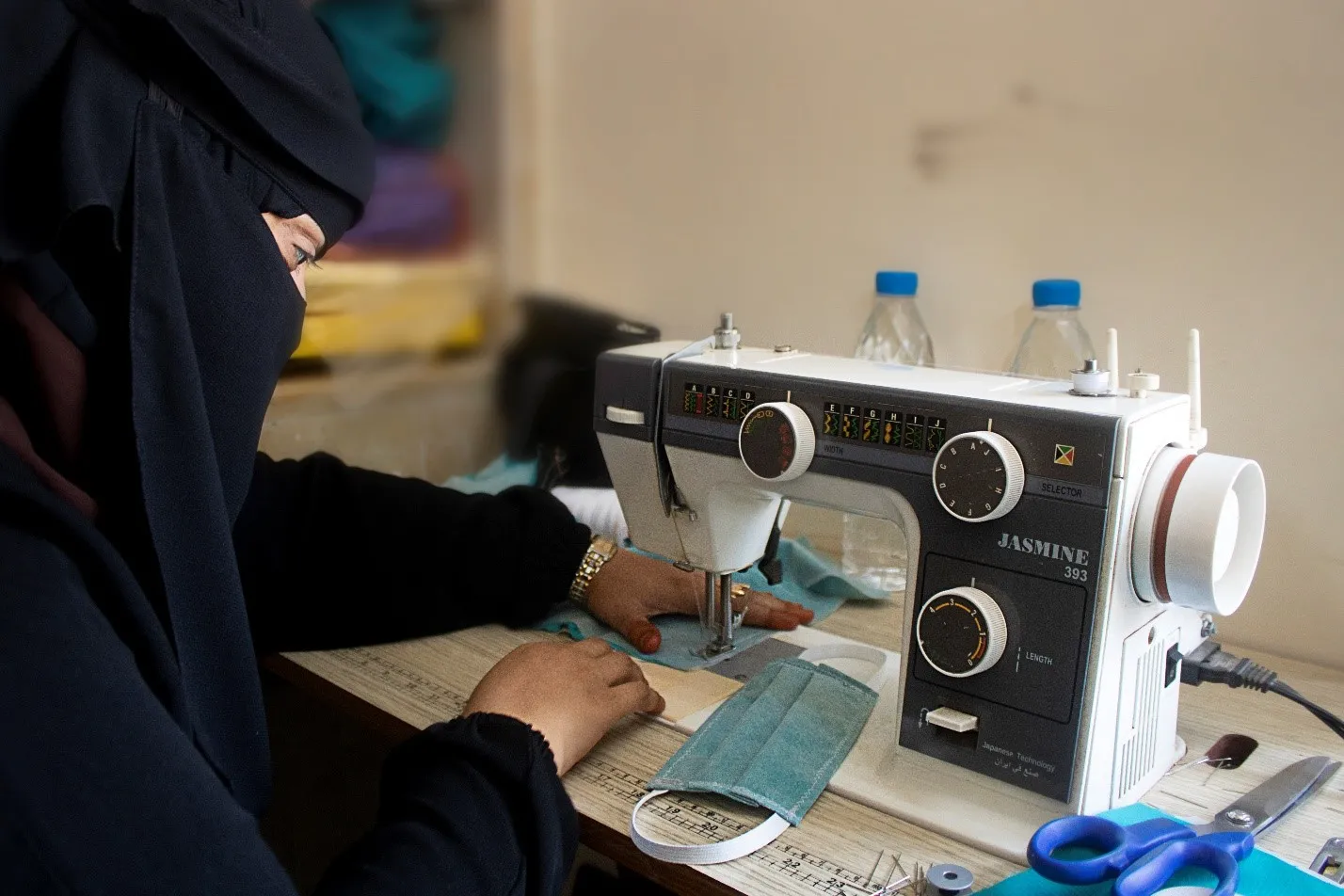 Una mujer yemení con un velo negro cose una máscara