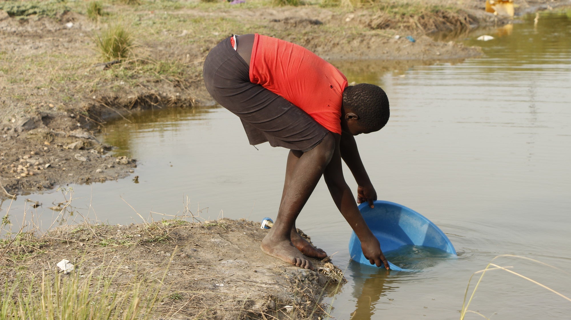 Mary is a widowed mother of six in South Sudan bends down to fill a bucket with water.