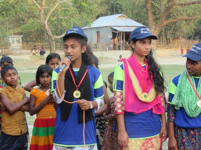 An adolescent girl with a microphone speaks to a group.