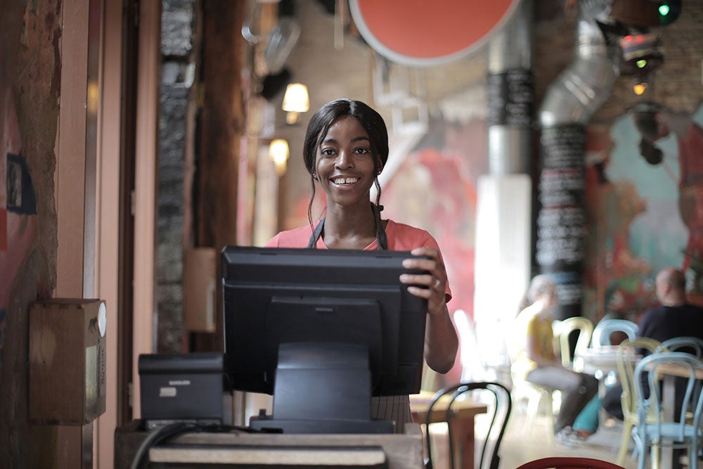 A young woman looks up from a register and smiles.