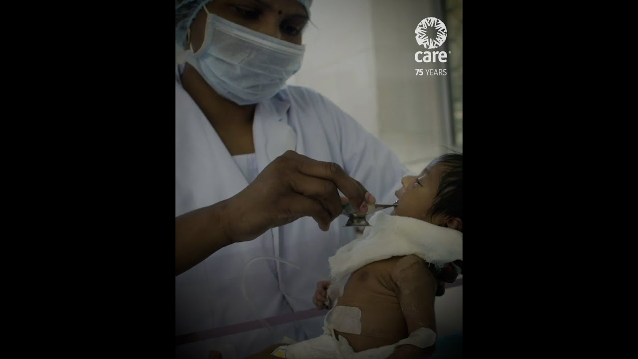 A preview image of a video showing a healthcare worker, wearing a facemask, helping a baby.