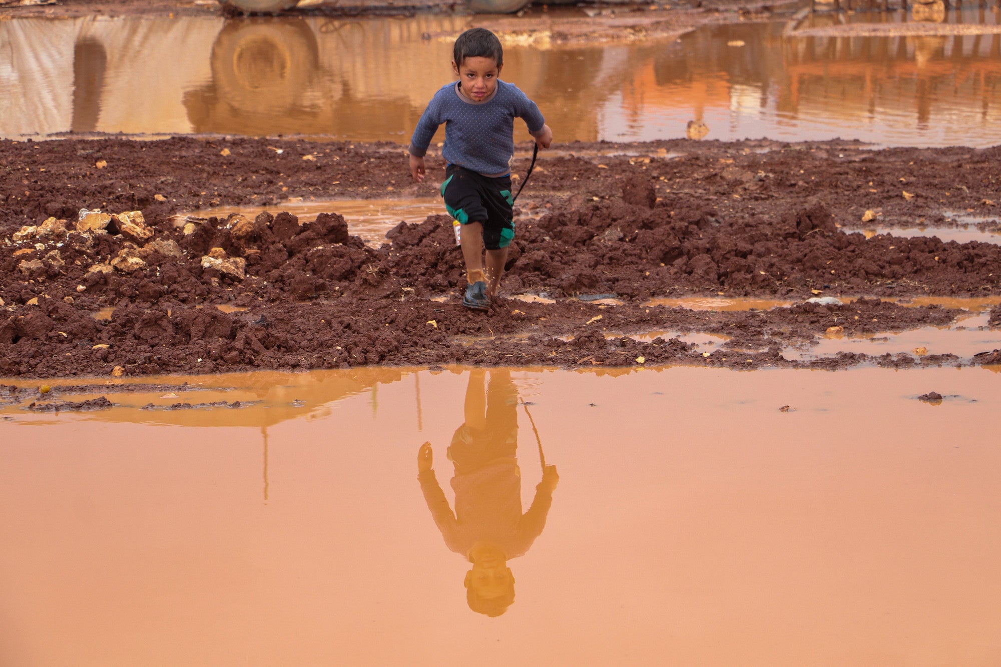 A small boy in a flooded camp in Syria runs towards a large puddle.