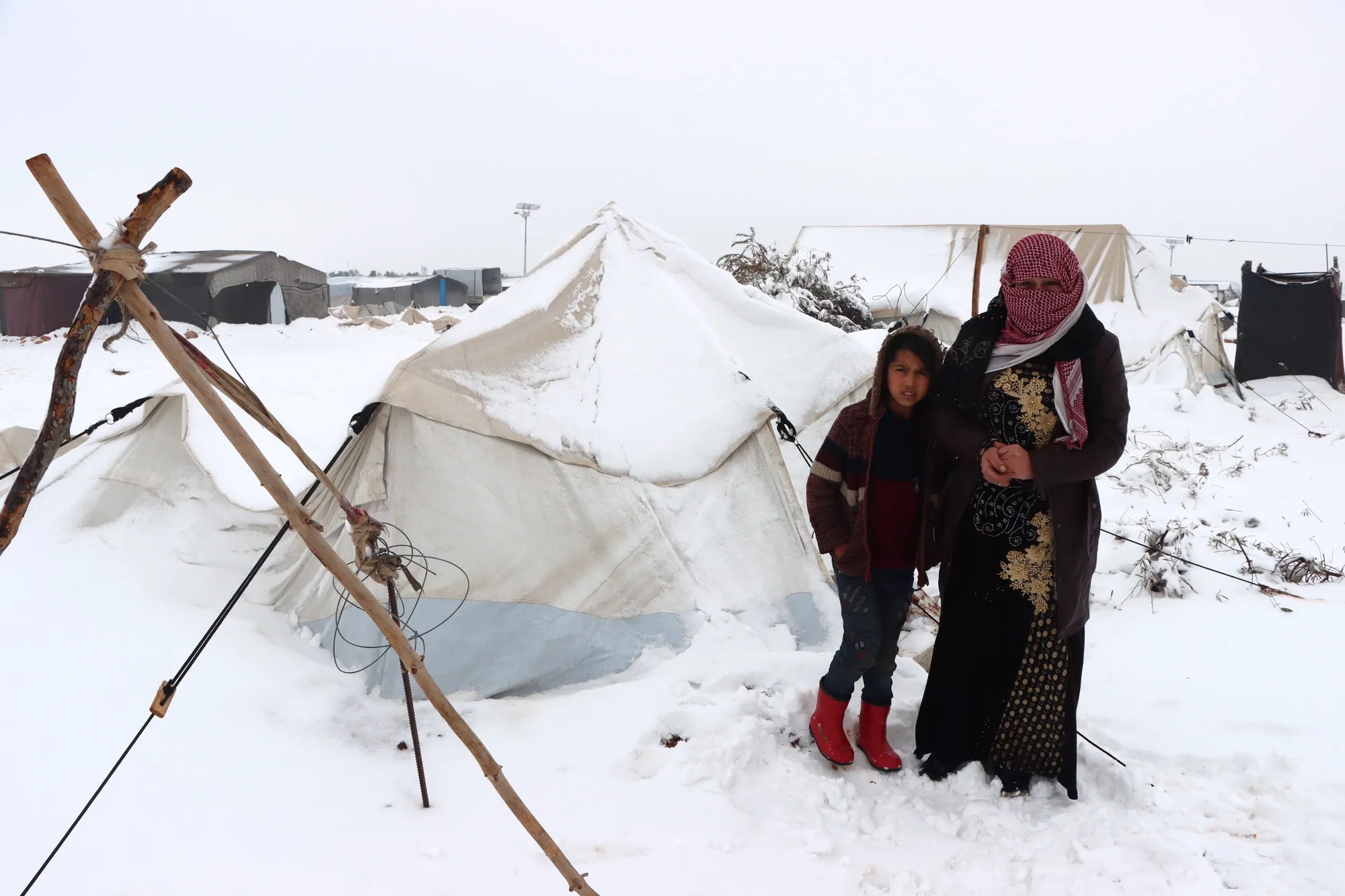 Duas pessoas do lado de fora de uma tenda coberta de neve em um acampamento na Síria
