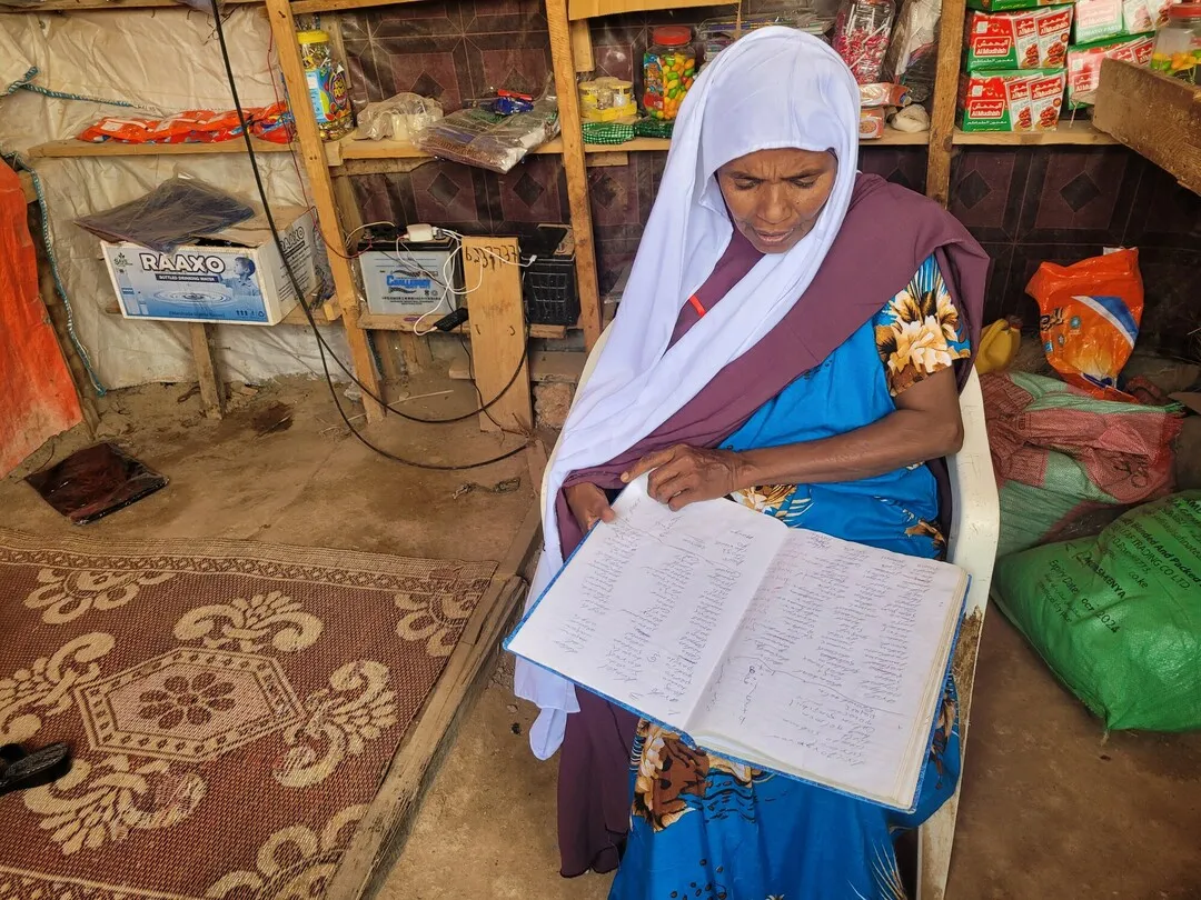 Ardo Dhunkel, de 60 años, en su pequeña tienda en un pueblo de Somalia mirando su libro con todos los préstamos.