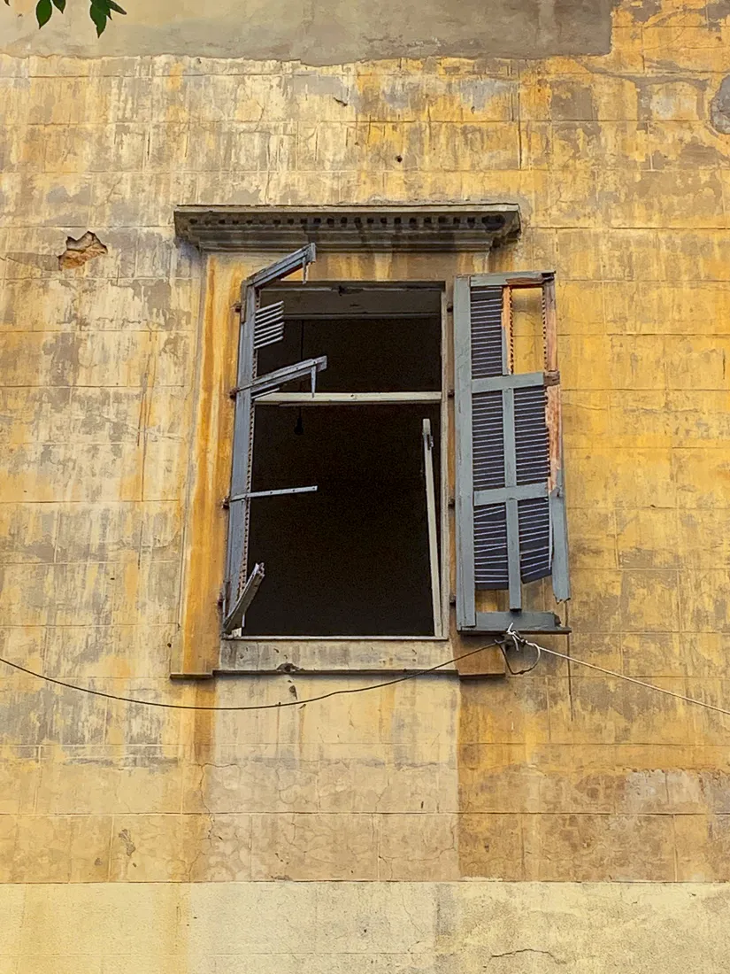Image of window with no glass and ragged shutters