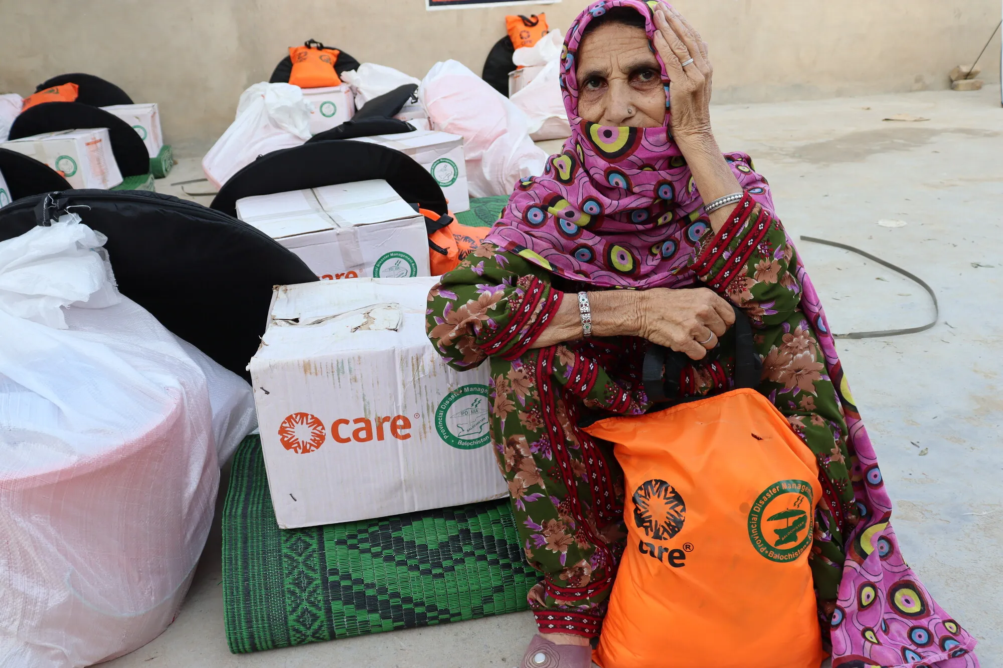 A woman affected by floods in Pakistan sits near emergency supplies supplied to her by CARE.