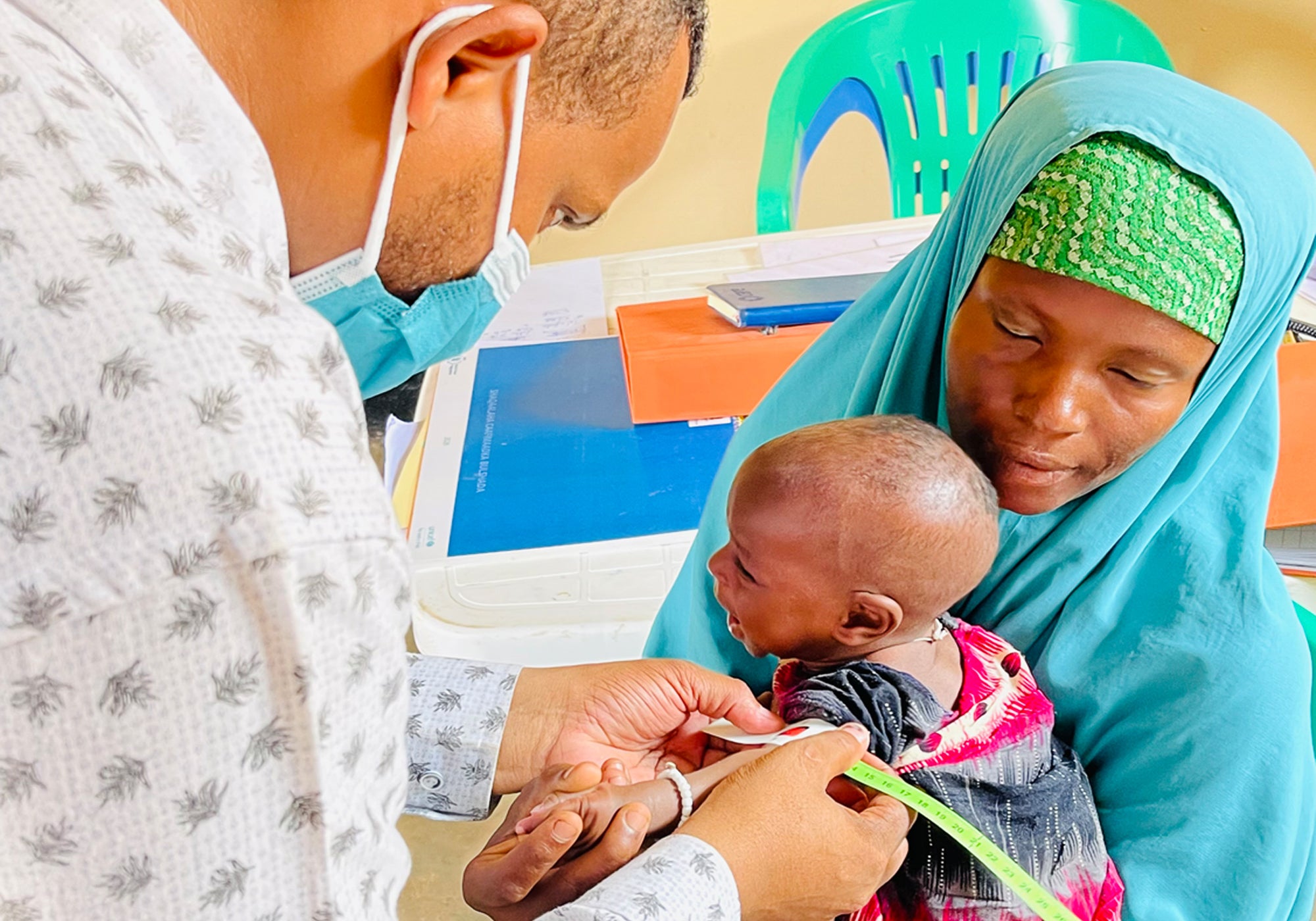 Une mère tient sa fille de 7 mois pendant que l'agent de santé Abdikadir Abukar mesure son tour de bras moyen (MUAC) au centre de santé de Kismayo.
