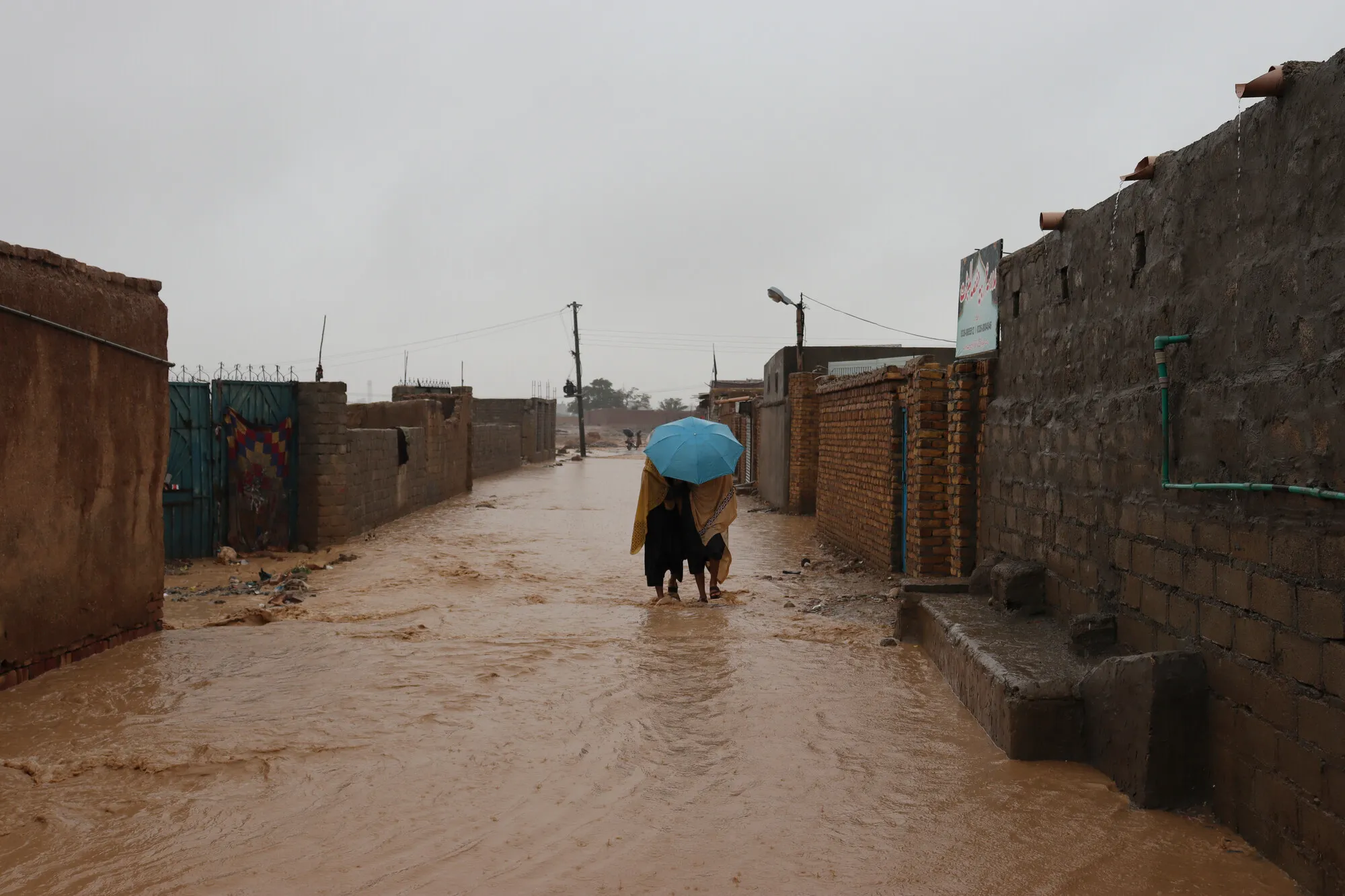 Pessoas andando nas águas da inundação, com guarda-chuva