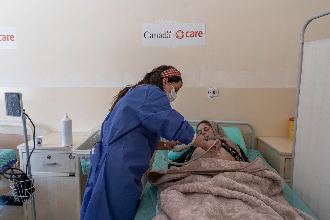 Una trabajadora de la salud que usa batas azules se inclina para ayudar a una mujer embarazada acostada en una cama de hospital.
