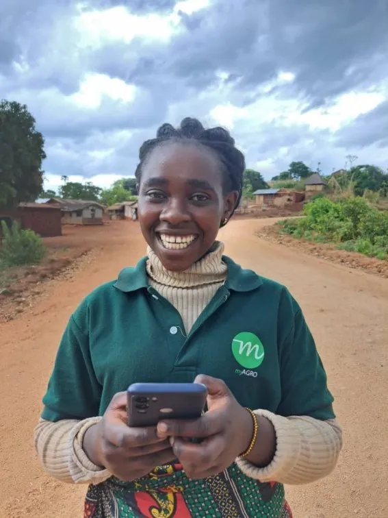 A woman wearing a green polo smiles while holding a smartphone in her hands.