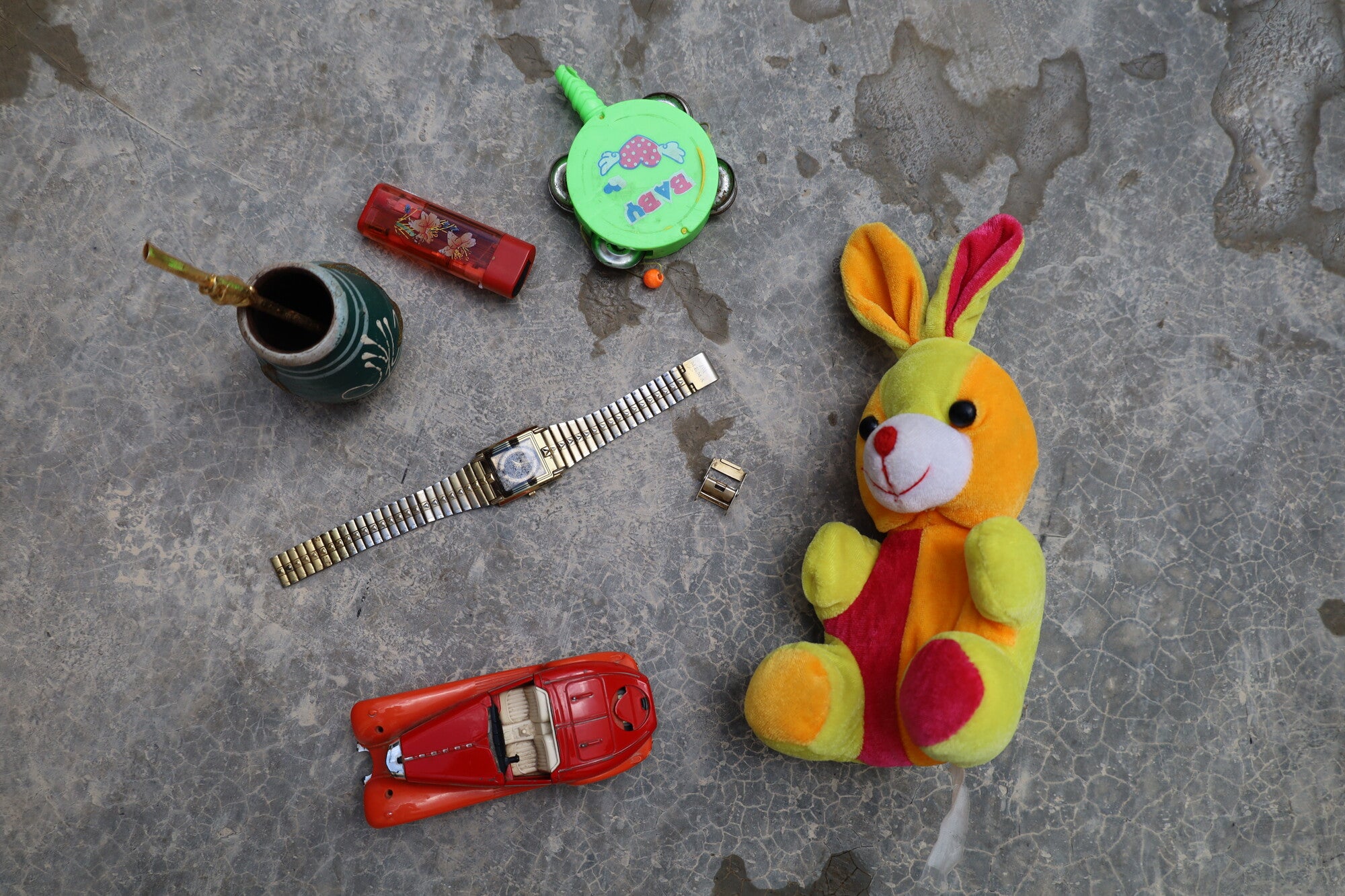 An assortment of objects, including a watch, stuffed rabbit, toy car, and mug with straw.