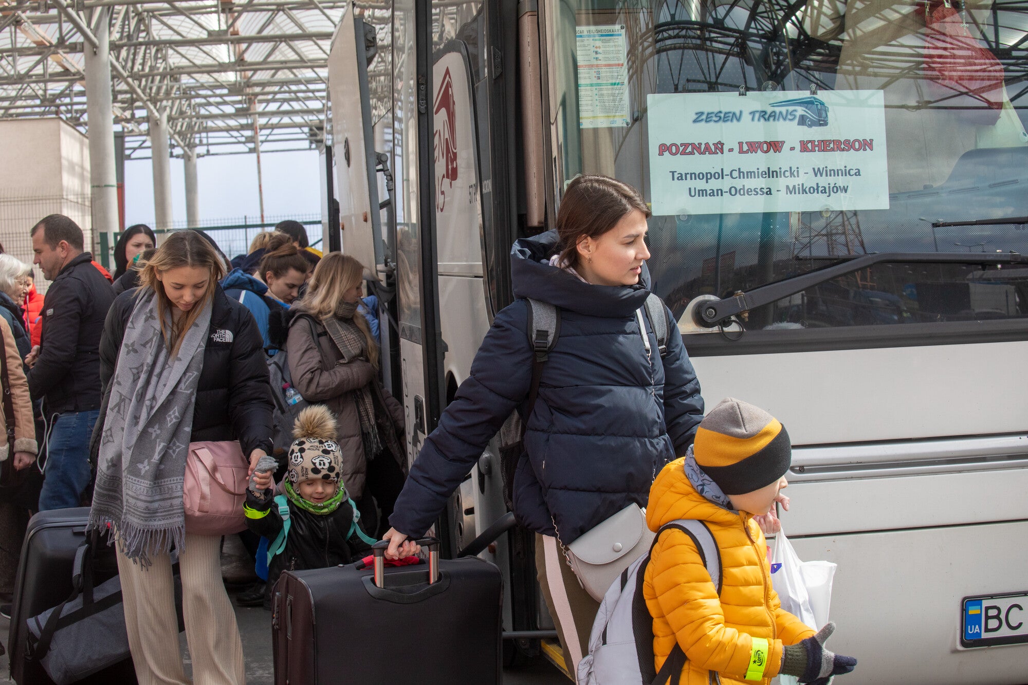 Ukrainian refugee woman with children steps off a bus with suitcases